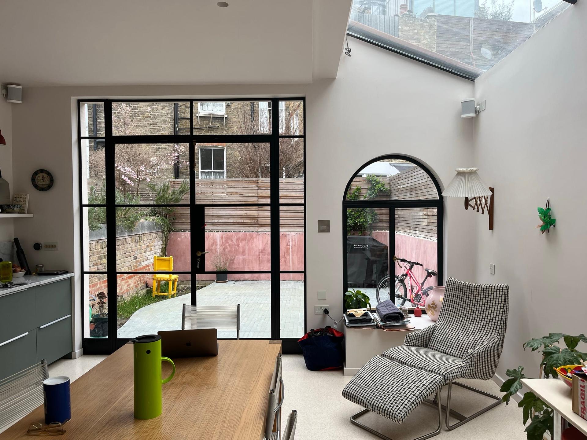 Kitchen and dining room under a rooflight, opening to the courtyard through steel glazing — Fieldway Crescent, Norbury SW16