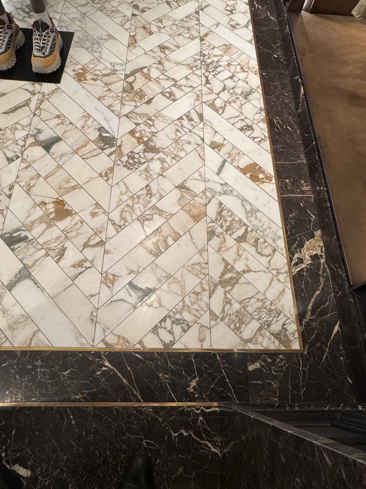 Calacatta chevron marble floor with a dark marble border and brass strip — Moncler, London