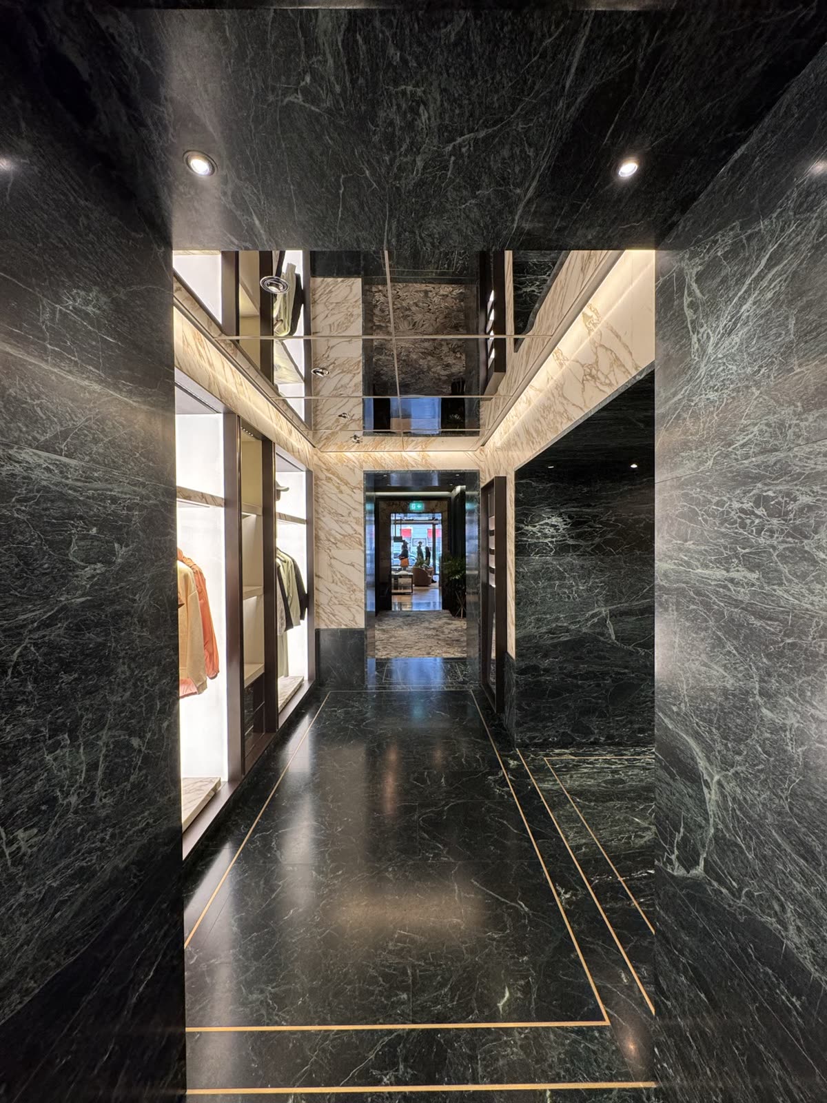 Green marble walls and floor with a brass inlay beneath a mirrored ceiling — Moncler, London