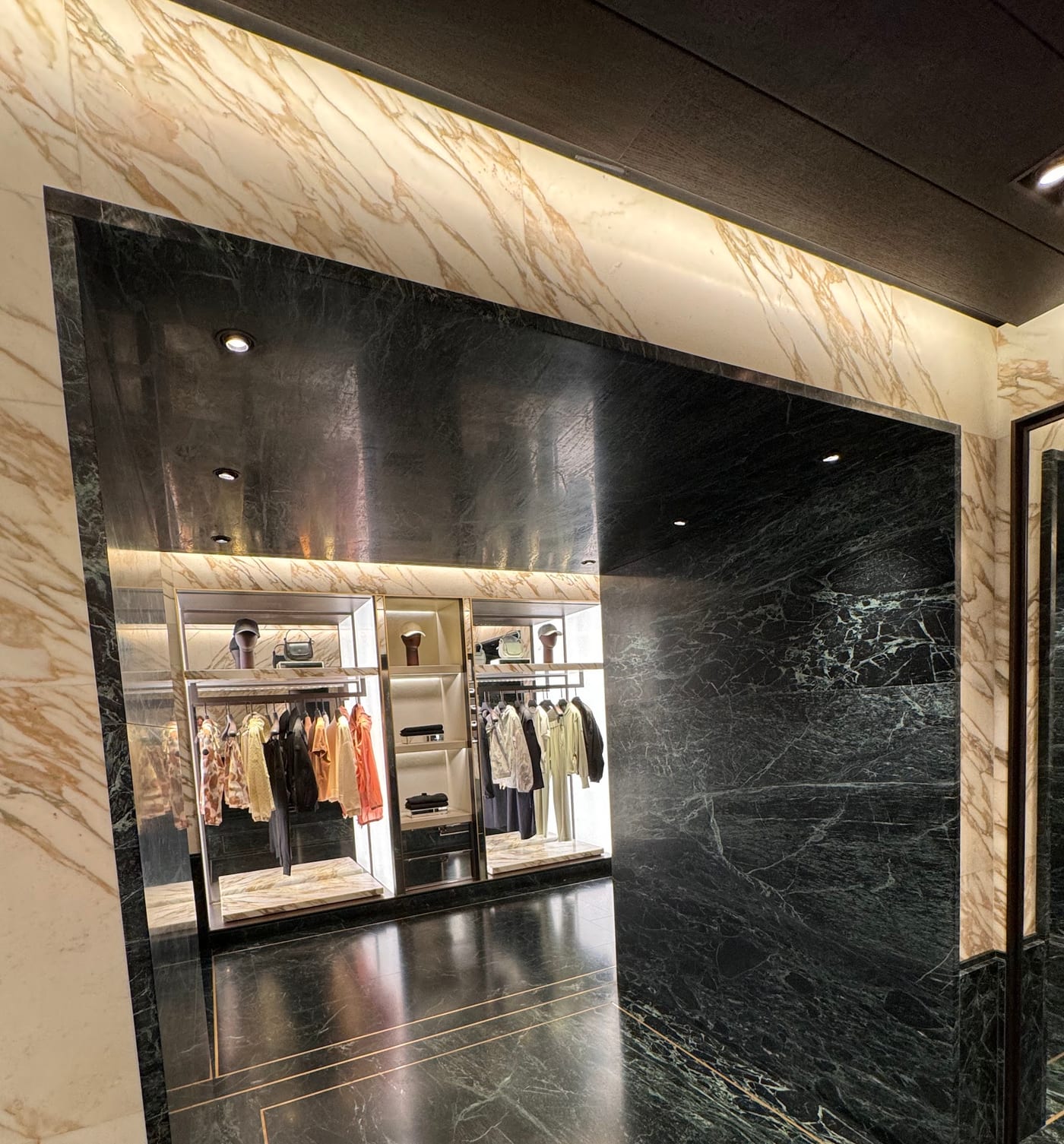Marble portal to a lit display bay — Moncler · London · verde alpi portal, illuminated niches
