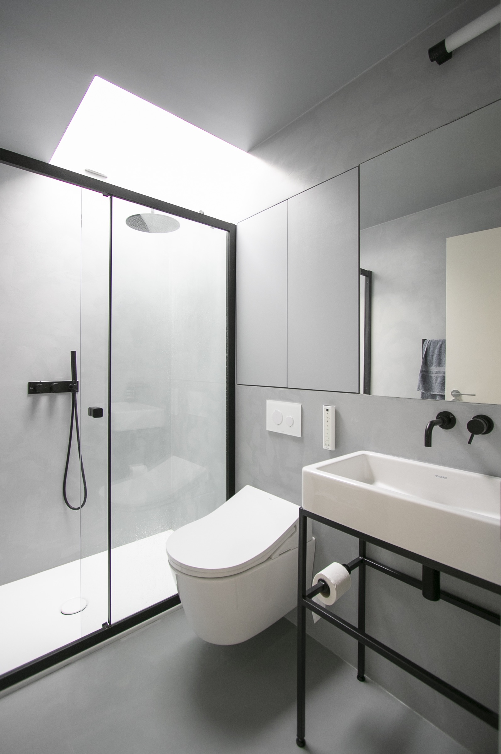 Microcement shower room — Seamless poured microcement walls and floor, matt black brassware, walk-in screen, skylight over