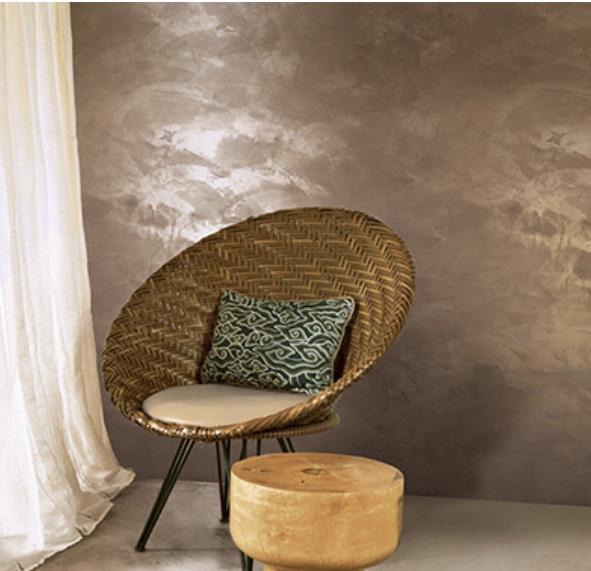 Bronze metallic wall with a light-reactive shimmer behind a woven rattan chair and a timber stool