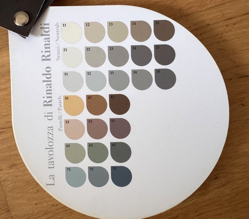 Round colour chart of twenty-seven numbered resin nuances, neutrals above and pastels below, held on a wooden table